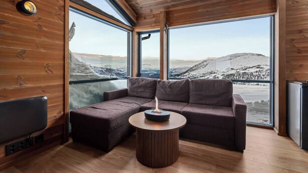 A cozy cabin with a wooden interior, a sofa, a small table, and a view of snowy mountains. - Exclusive cabin and annex at the top of Hodlekve (Vestland)