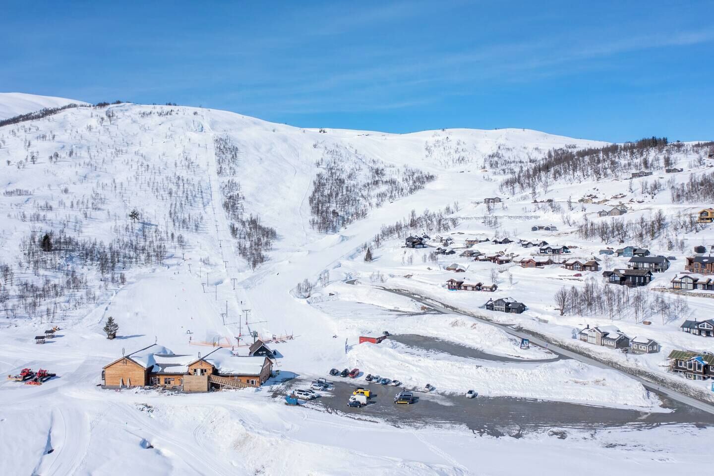 A snow-covered mountain village with a ski resort, including a lodge, parking area, and ski lifts.