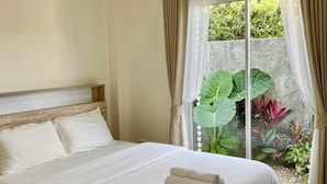 Ein Schlafzimmer mit Bett, Deckenventilator und Blick auf Grün hinter einer Schiebetür.