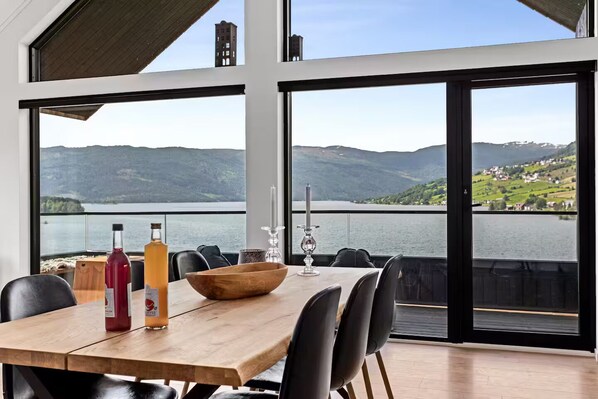 Un espace repas avec une table en bois, des chaises et une vue sur un lac et des montagnes.