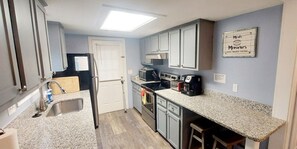 A compact kitchen with granite countertops, a refrigerator, a microwave, and a coffee maker. - Totally Renovated 3-Bedroom Beach House across from the Ocean! (Myrtle Beach)
