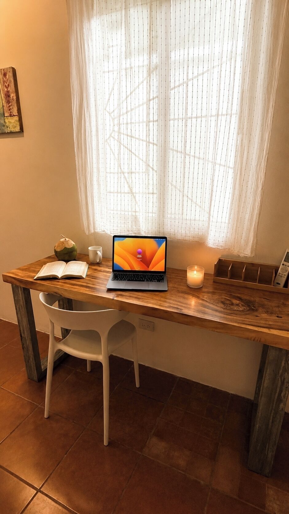 Un escritorio de madera con una computadora portátil, un libro abierto, una vela y un adorno.