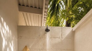 Un petit espace douche fermé, avec une planche de surf appuyée contre le mur.