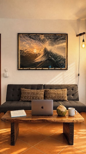 Un salon moderne avec un canapé gris, une table basse en bois, un ordinateur portable, un livre, une noix de coco et une lampe.