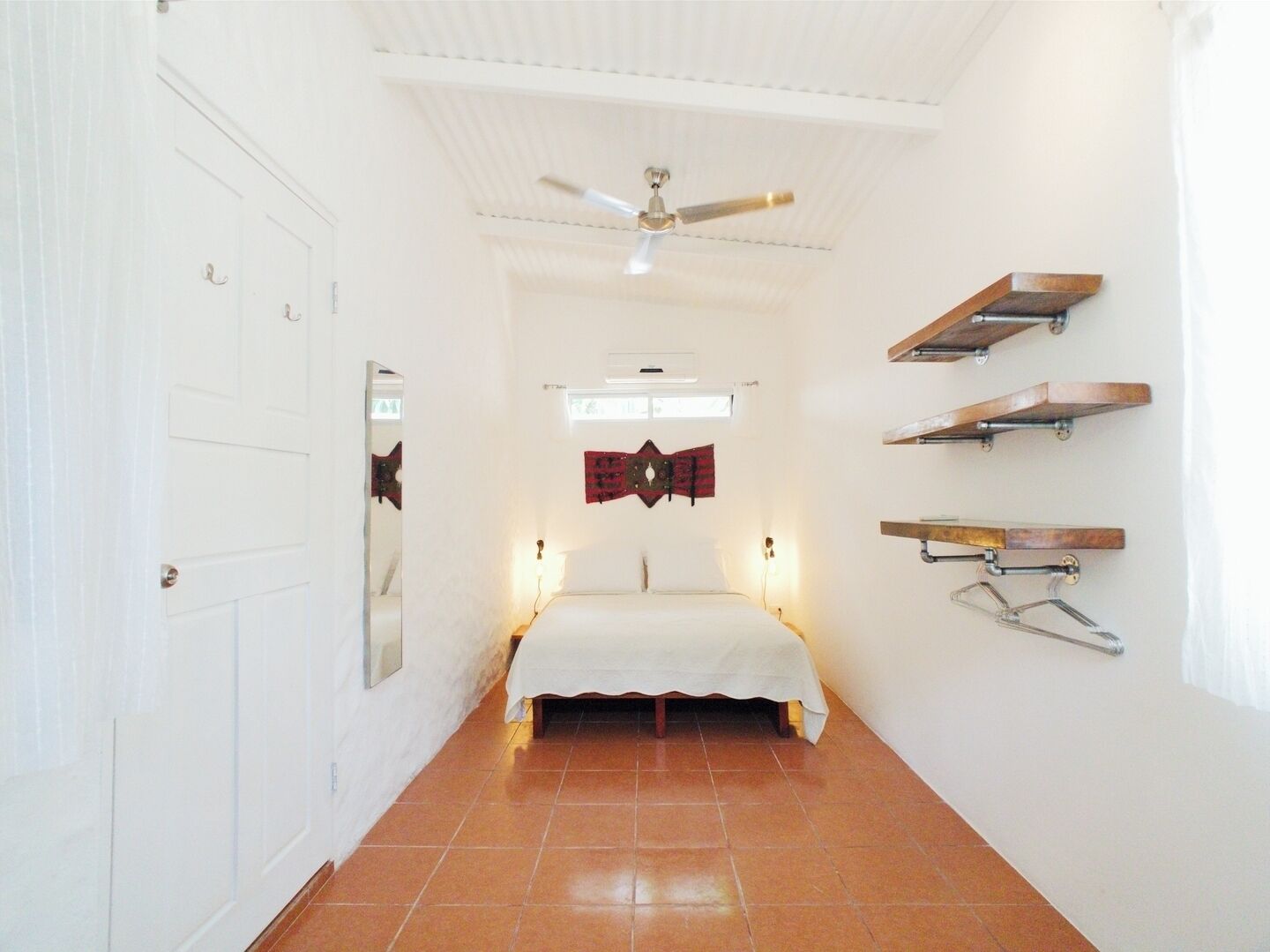 A narrow hallway leading to a bed with a ceiling fan, white walls, and a tiled floor.