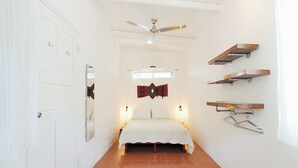 Un couloir étroit mène à une chambre avec un ventilateur de plafond, des murs blancs et un sol carrelé.