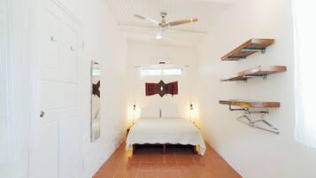 A narrow hallway leading to a bed with a ceiling fan, white walls, and a tiled floor.