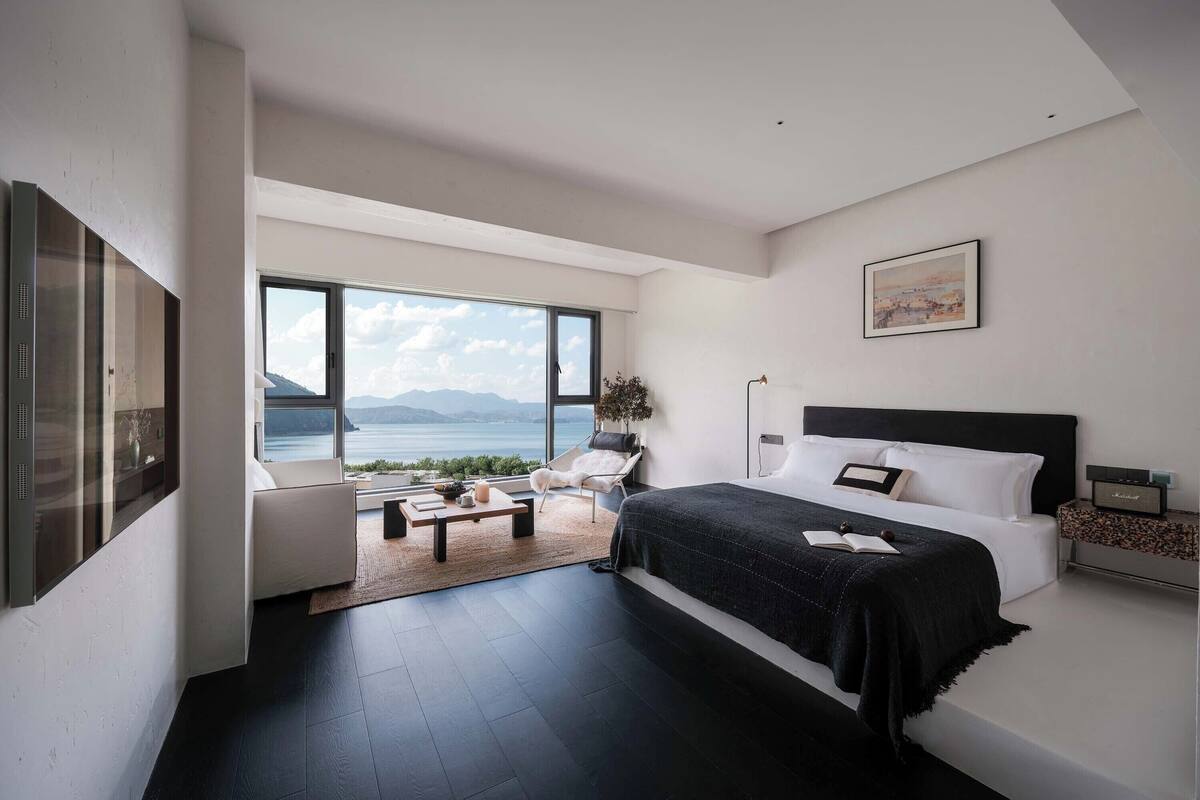 Ein modernes Schlafzimmer mit großem Fenster, einem Bett, einer Couch und einem Couchtisch.