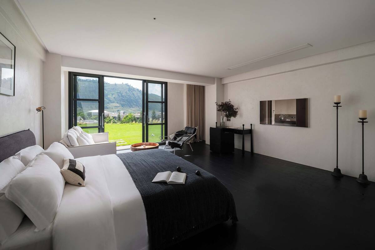 Ein modernes Hotelzimmer mit einem großen Bett, einem Schreibtisch, einem Stuhl und Blick ins Freie.