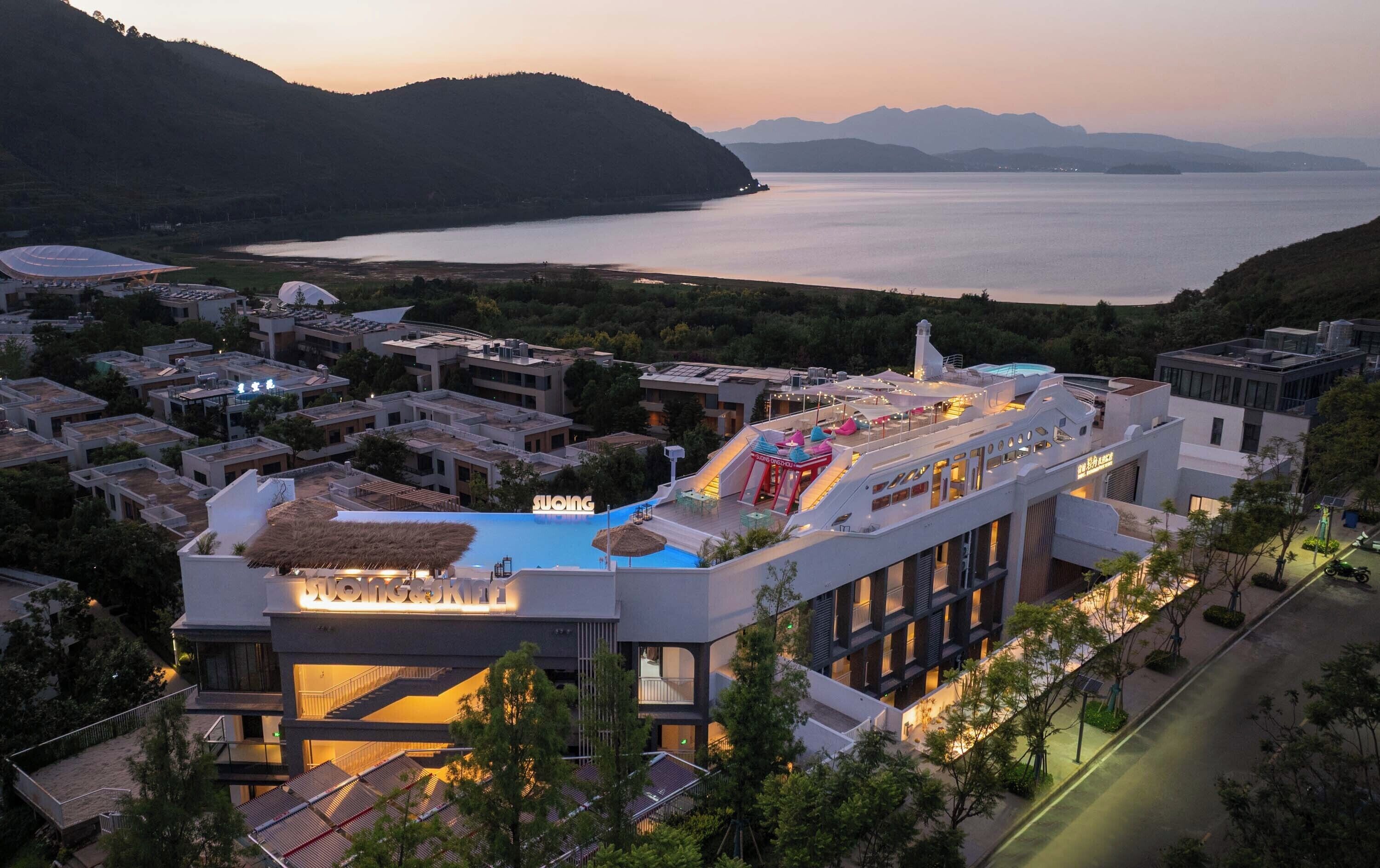 A modern hotel with a rooftop pool, multiple floors, and a scenic view of a lake and mountains.