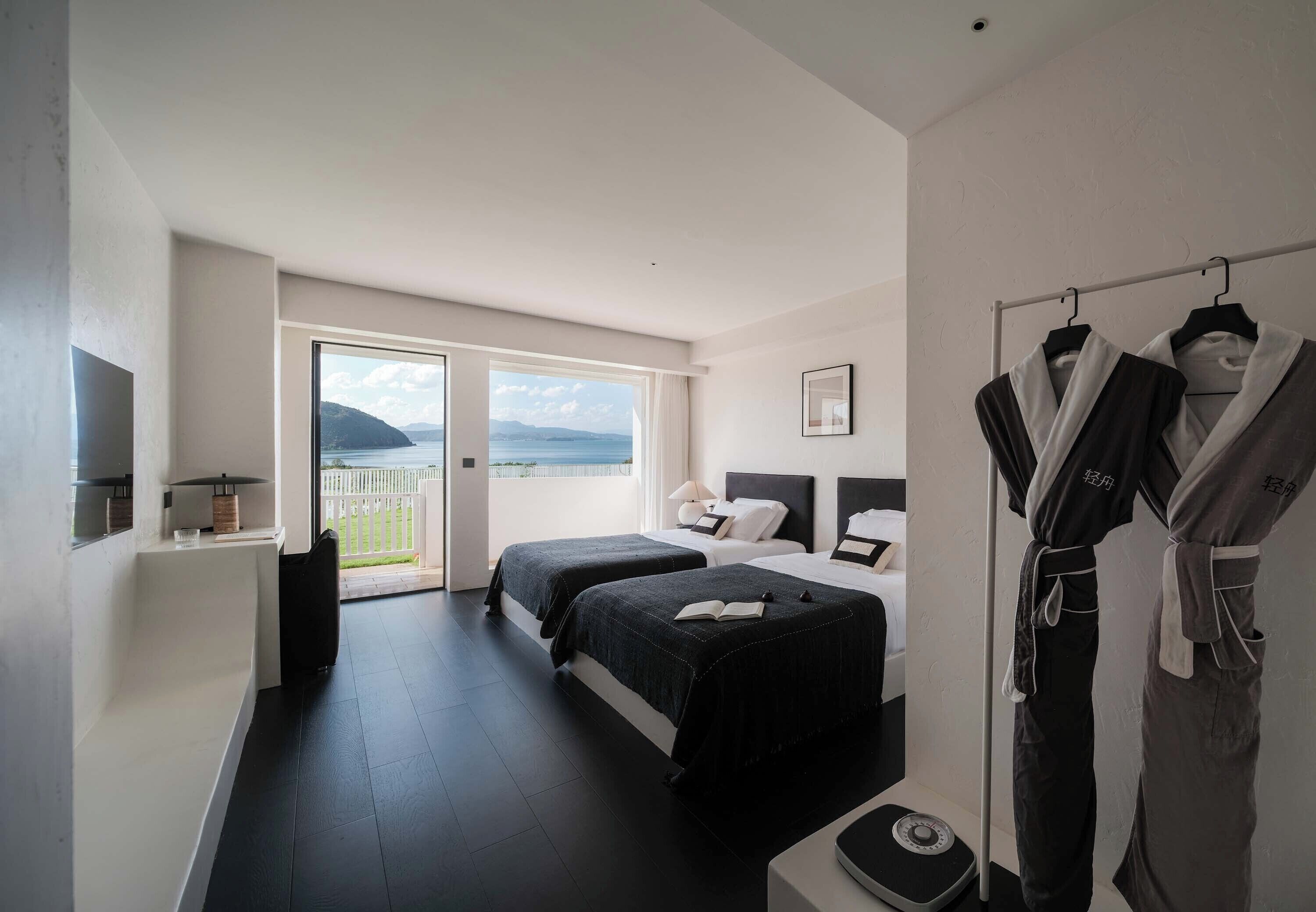 A hotel room with two beds, a large window with a view of the sea, a wardrobe, and a scale on the floor.