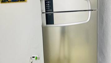 A stainless steel refrigerator with a control panel, a power cord, and a wall-mounted picture.