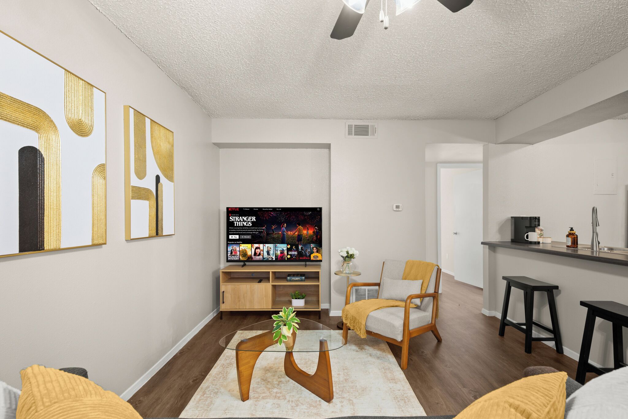 A modern living room with a TV, seating, and a kitchen area.