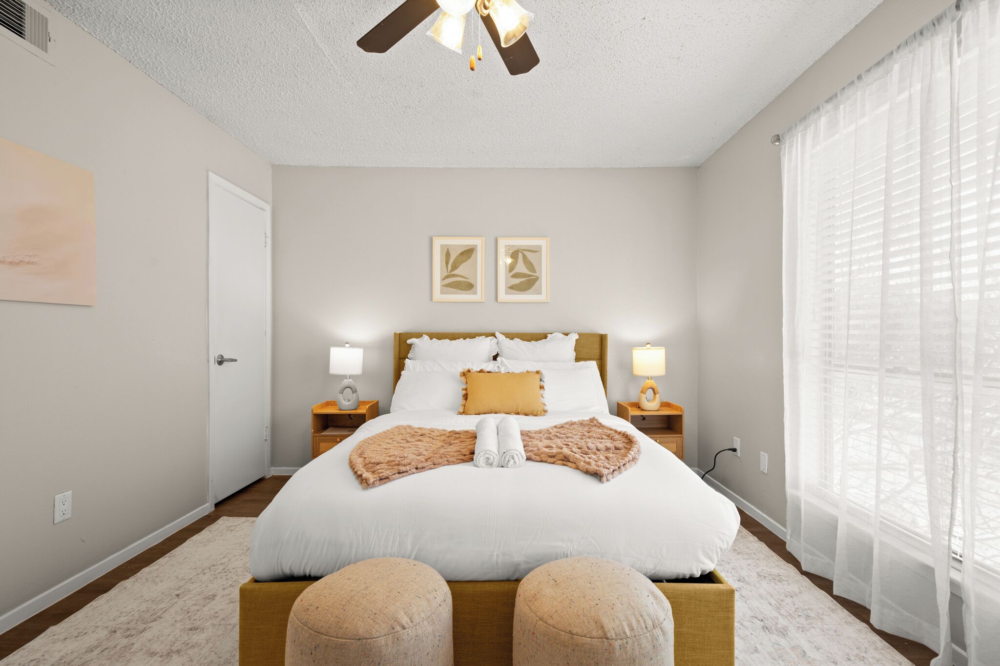 A neatly arranged bedroom with a large bed, bedside lamps, and a ceiling fan.