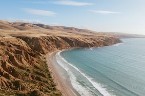 A coastal landscape with a curved shoreline, sandy beach, and rugged cliffs.