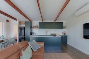 A modern kitchen with a central island, built-in cabinets, and a dining area with a sofa and chairs. - Soul Shack | Pet Friendly + Steps to Beach (Aldinga Beach)