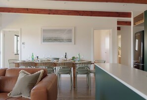 A modern dining area with a wooden table, chairs, and a view of the sea through a large window.