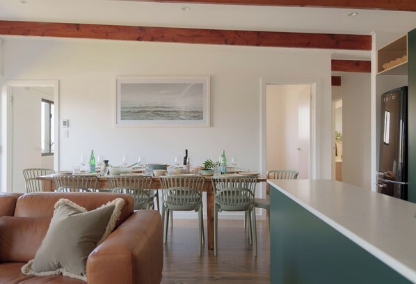 A modern dining area with a wooden table, chairs, and a view of the sea through a large window.