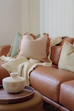 A brown leather sofa with a white vase on a round wooden table. - Soul Shack | Pet Friendly + Steps to Beach (Aldinga Beach)