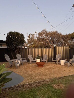 An outdoor seating area with chairs and a table, surrounded by a fence and string lights.