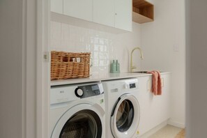 A compact laundry area with a washing machine, a dryer, a sink, and a wicker basket on the countertop.
