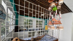 Una stanza con soffitto in legno, una finestra vista, un tavolo con tovaglia a motivi blu e vasi di terracotta appesi.