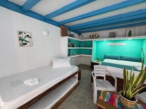 Une pièce comprenant un lit, un bureau et une chaise. On y trouve des étagères remplies d’objets, ainsi qu’un panneau accroché au mur.