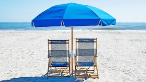 Due sedie da spiaggia sotto un ombrellone blu su una spiaggia sabbiosa, con l'oceano sullo sfondo.