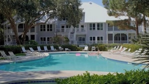Una piscina con lettini, circondata da alberi e un grande edificio con balconi.