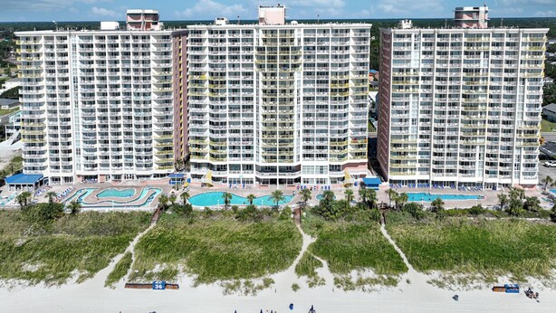 Un hotel de altura con múltiples balcones, una zona de piscina y vista a la playa.
