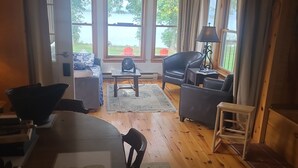 A cozy room with a dining table, chairs, a sofa, and a window overlooking a scenic outdoor area.