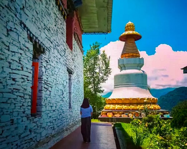 A person walking past a stone building with a traditional structure in the background. - Yangsum Village Homestay (Gyalshing)