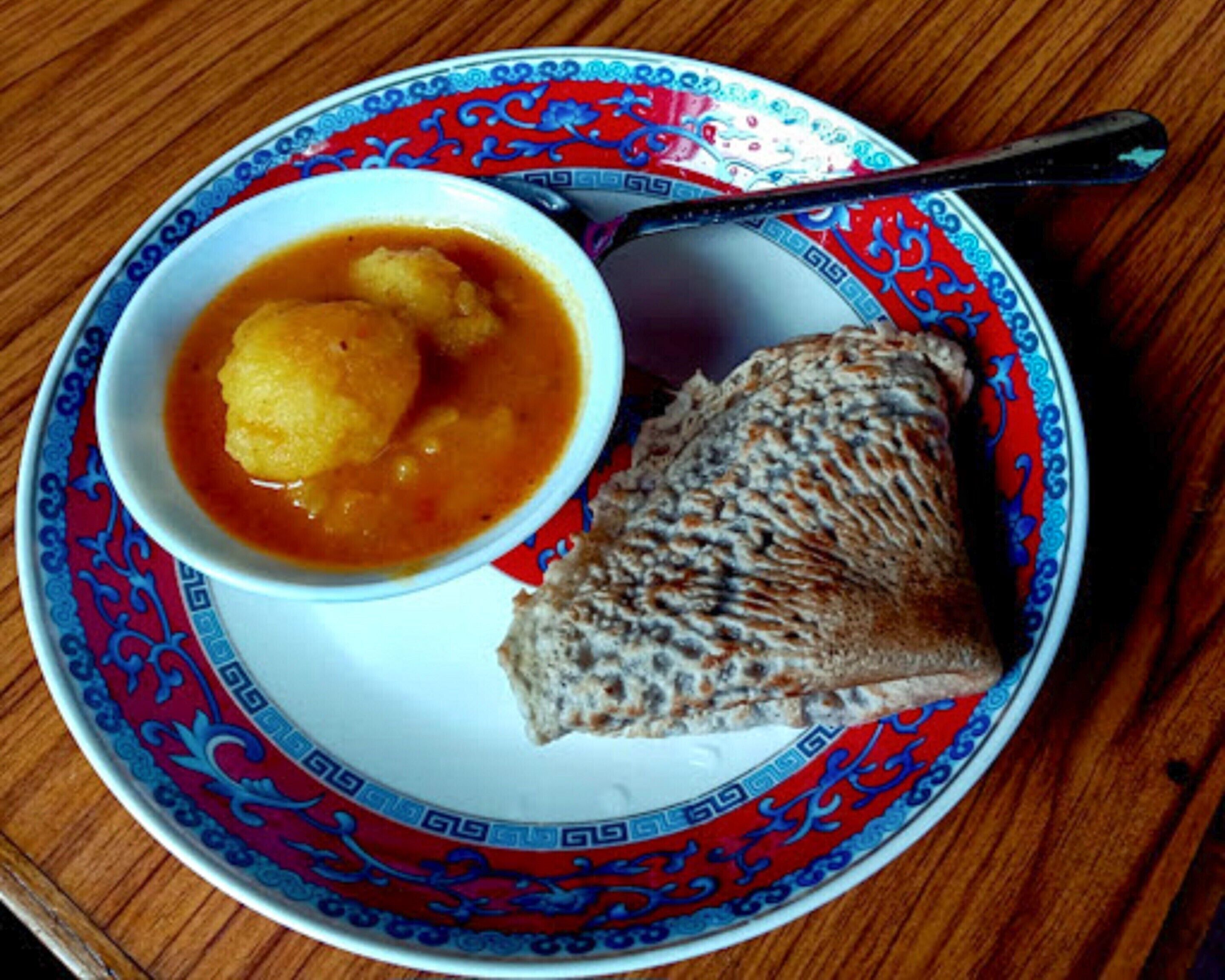 Un plat amb un bol de sopa i una llesca de pa sobre un plat decoratiu.