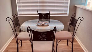 A dining area with a round table, four chairs, and a window with blinds. - Surf Shack Across from the Beach (Cocoa Beach)