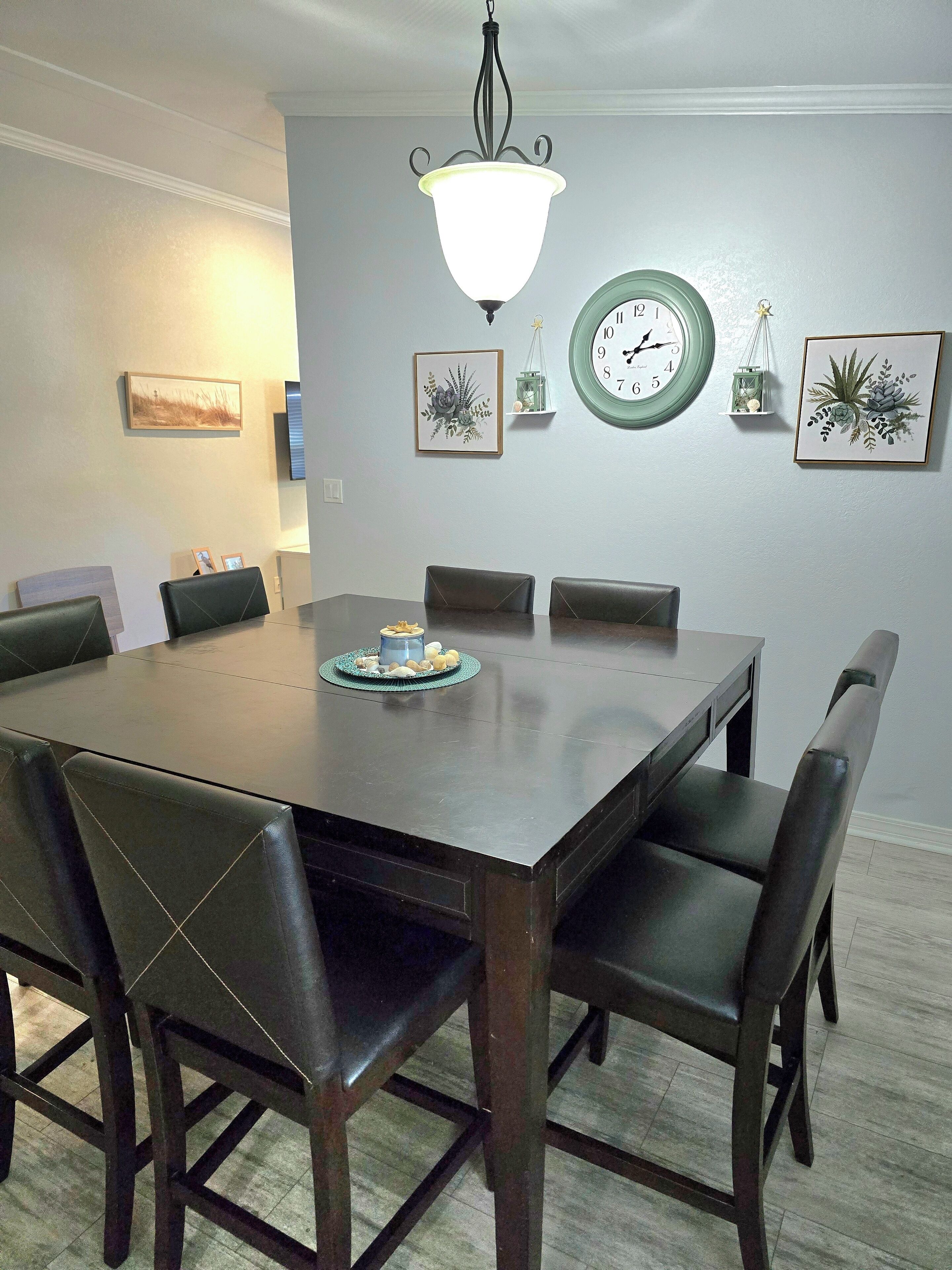 Un comedor con una mesa rectangular, seis sillas, un reloj de pared y cuadros enmarcados.