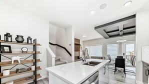 Une cuisine moderne dotée d’un îlot central, d’étagères en bois et d’un escalier menant à un espace repas.