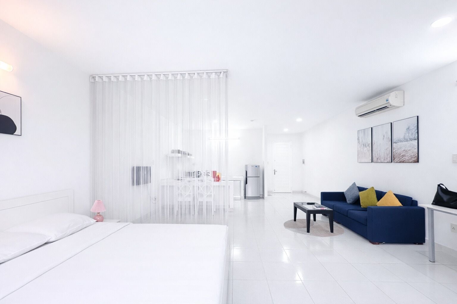 A modern hotel room with a bed, a blue sofa, a coffee table, and a kitchenette area.