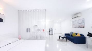A modern hotel room with a bed, a blue sofa, a coffee table, and a kitchenette area.