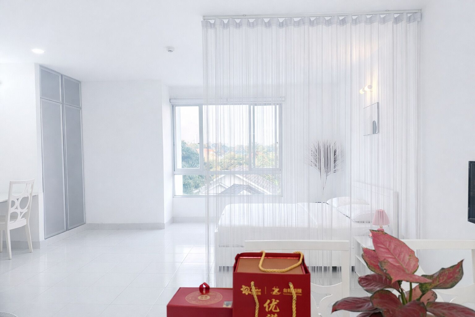 Una habitación moderna y minimalista con un ventanal grande, una silla blanca, una mesita pequeña y una planta decorativa.