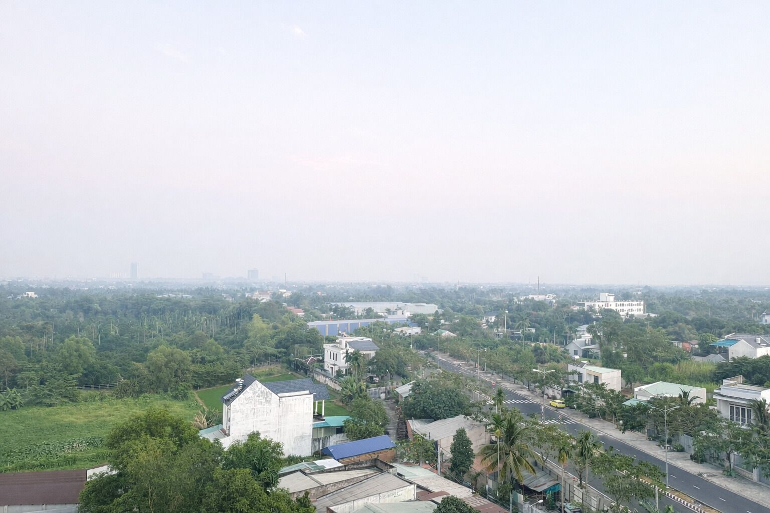 A residential area with a mix of single and multi-story houses, surrounded by greenery and a clear sky.