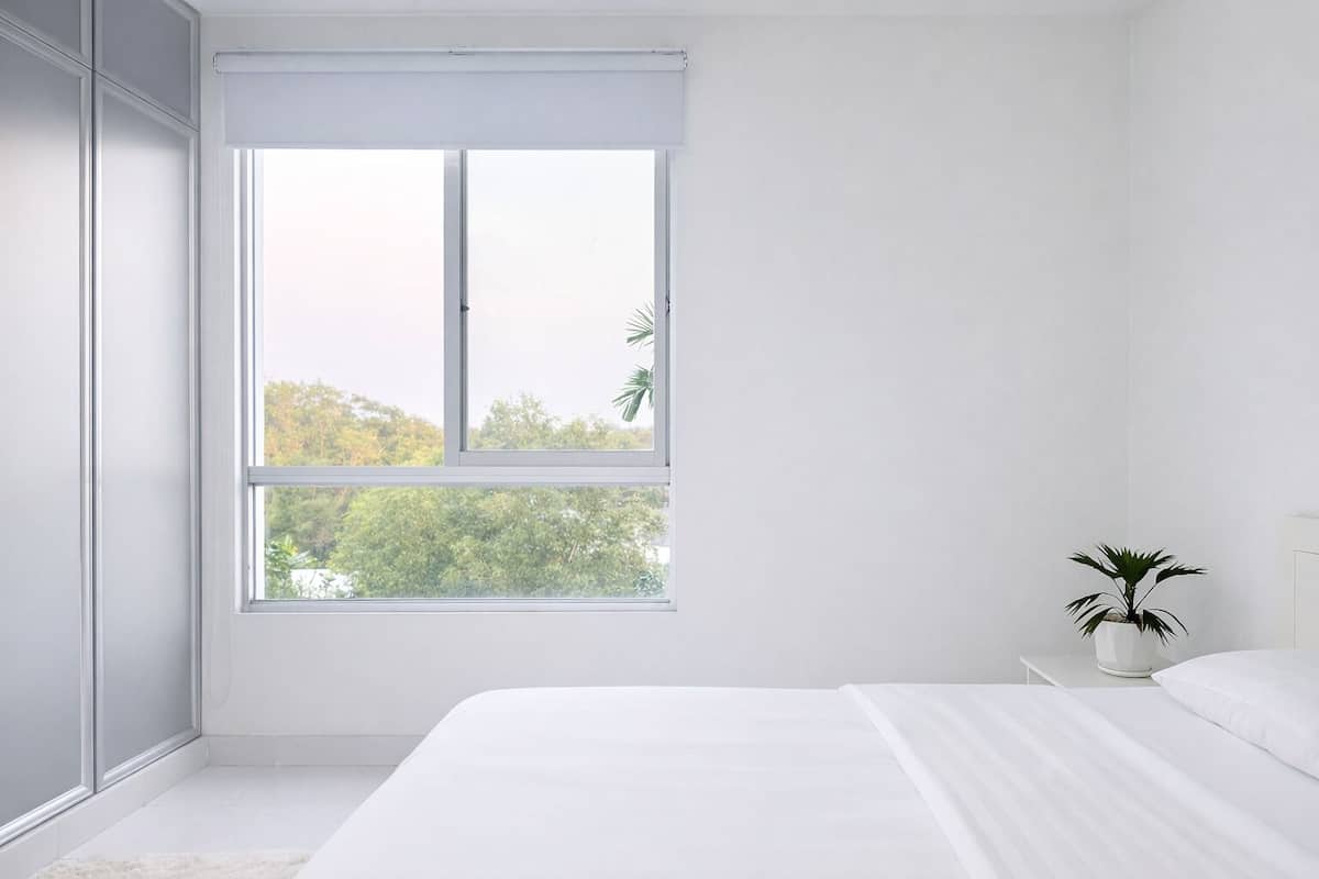 A minimalist bedroom with a large window, a bed, and a potted plant.