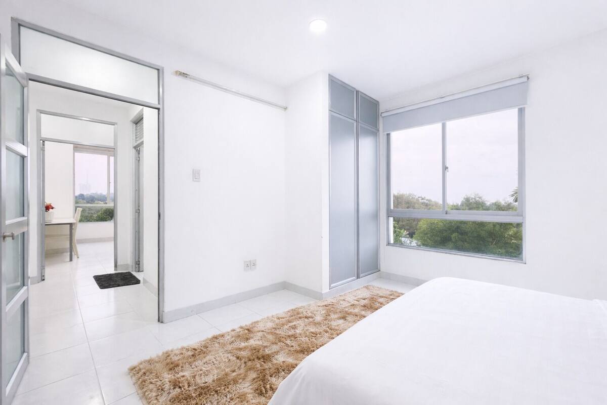 A modern bedroom with a large window, a bed, and a view of greenery outside.