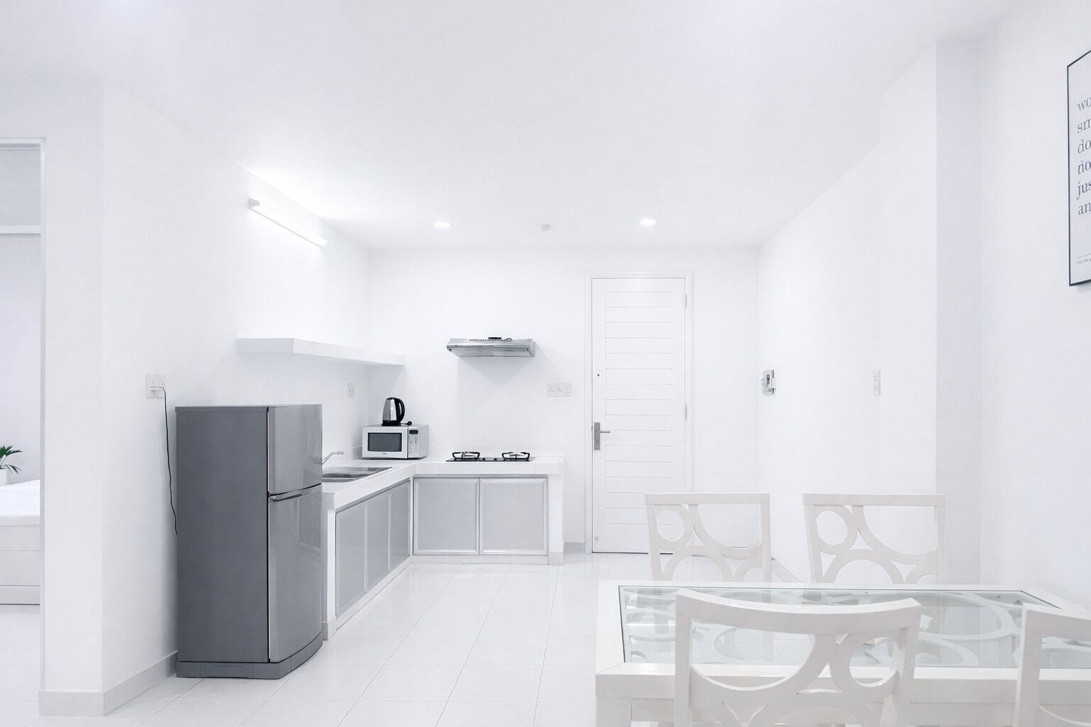 Une cuisine moderne avec des meubles blancs, un réfrigérateur, un four à micro-ondes et une cuisinière à gaz.