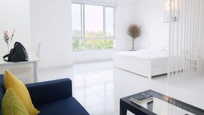 A modern hotel room with a large bed, a blue sofa, a small table, and a window with a view of greenery. - HD Garden Thu Dau Mot (Ho Chi Minh City)