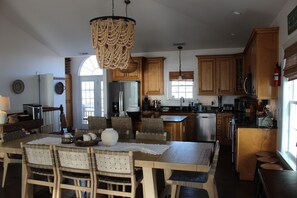 A spacious kitchen with wooden cabinets, a dining area with wicker chairs, and a large chandelier. - Private Five Bedroom Beach House furnished to maximize bedspace for everyone (North Topsail Beach)