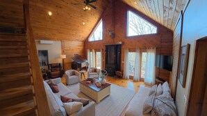 A spacious cabin with a high ceiling, wooden walls, a fireplace, a piano, and a cozy seating area.