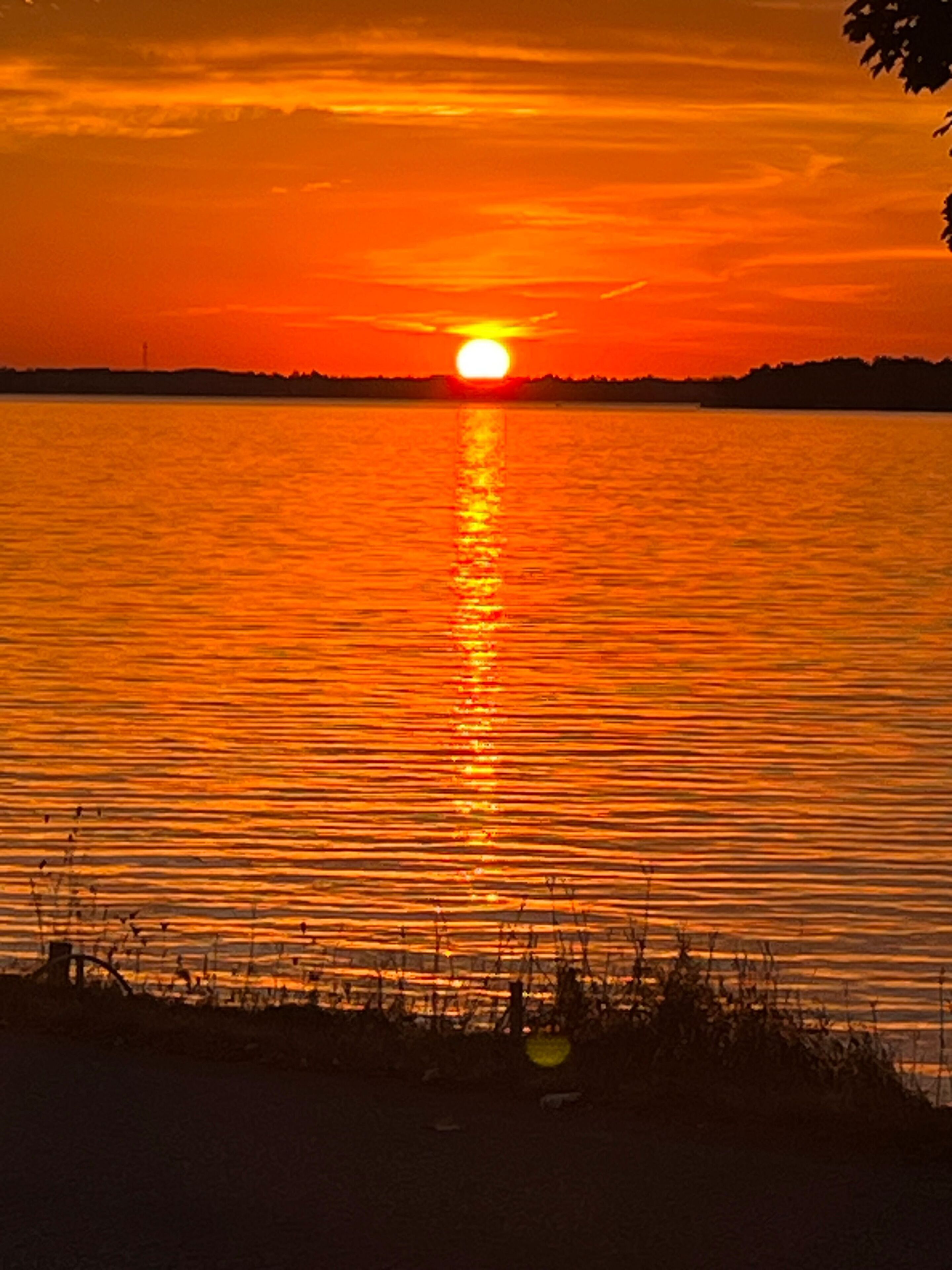 A sunset over a calm body of water with a silhouette of land in the distance.