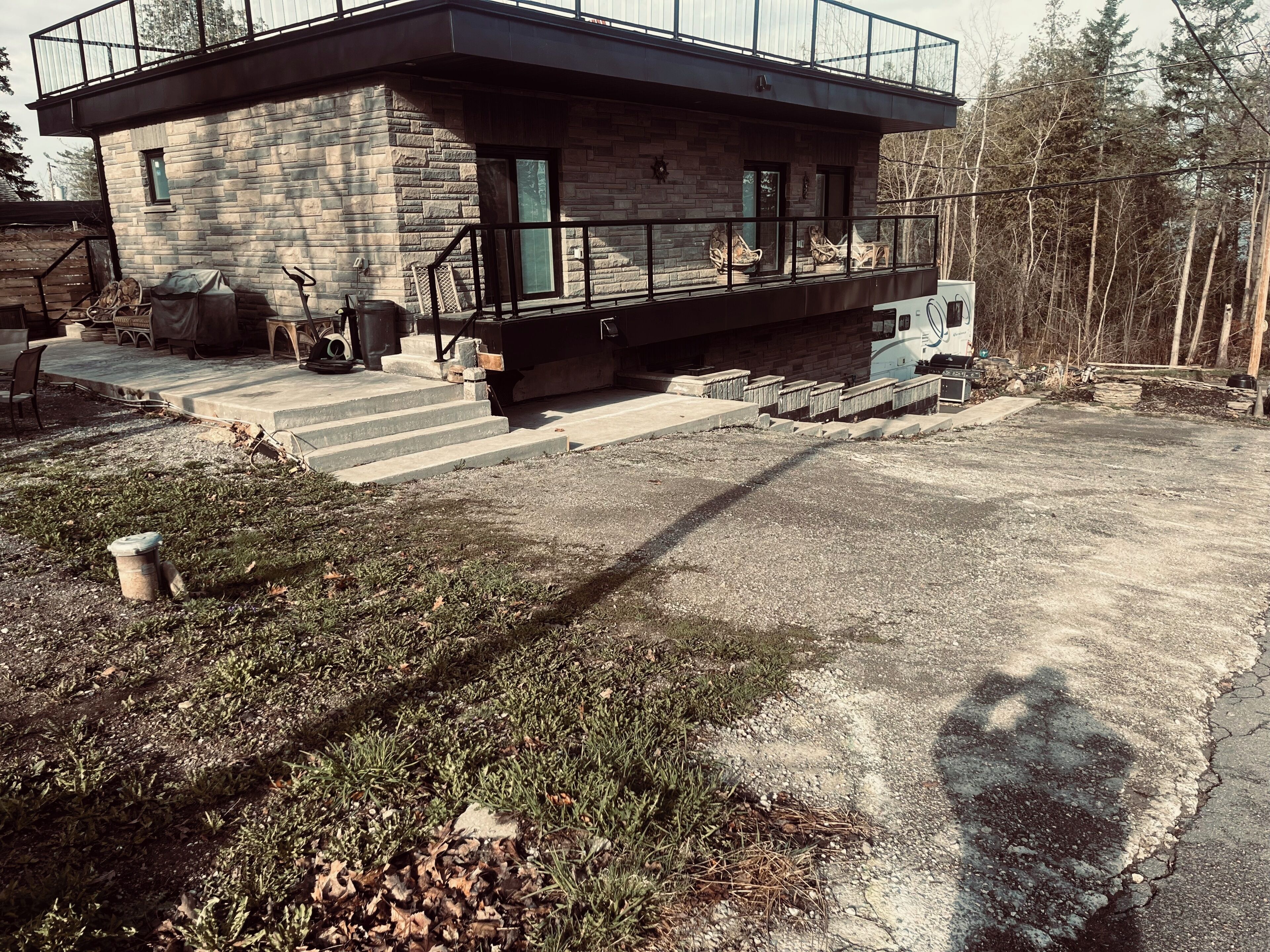 Una casa moderna de dos pisos con fachada de piedra, un balcón con mobiliario exterior y un camino de entrada.