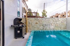 A swimming pool with a stone wall and a barbecue grill.
