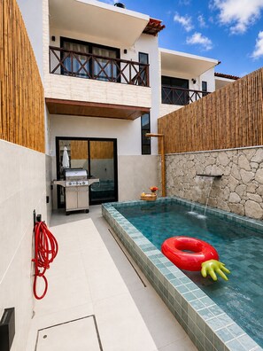 A modern outdoor pool area with a stone wall, a barbecue grill, and a red inflatable ring.